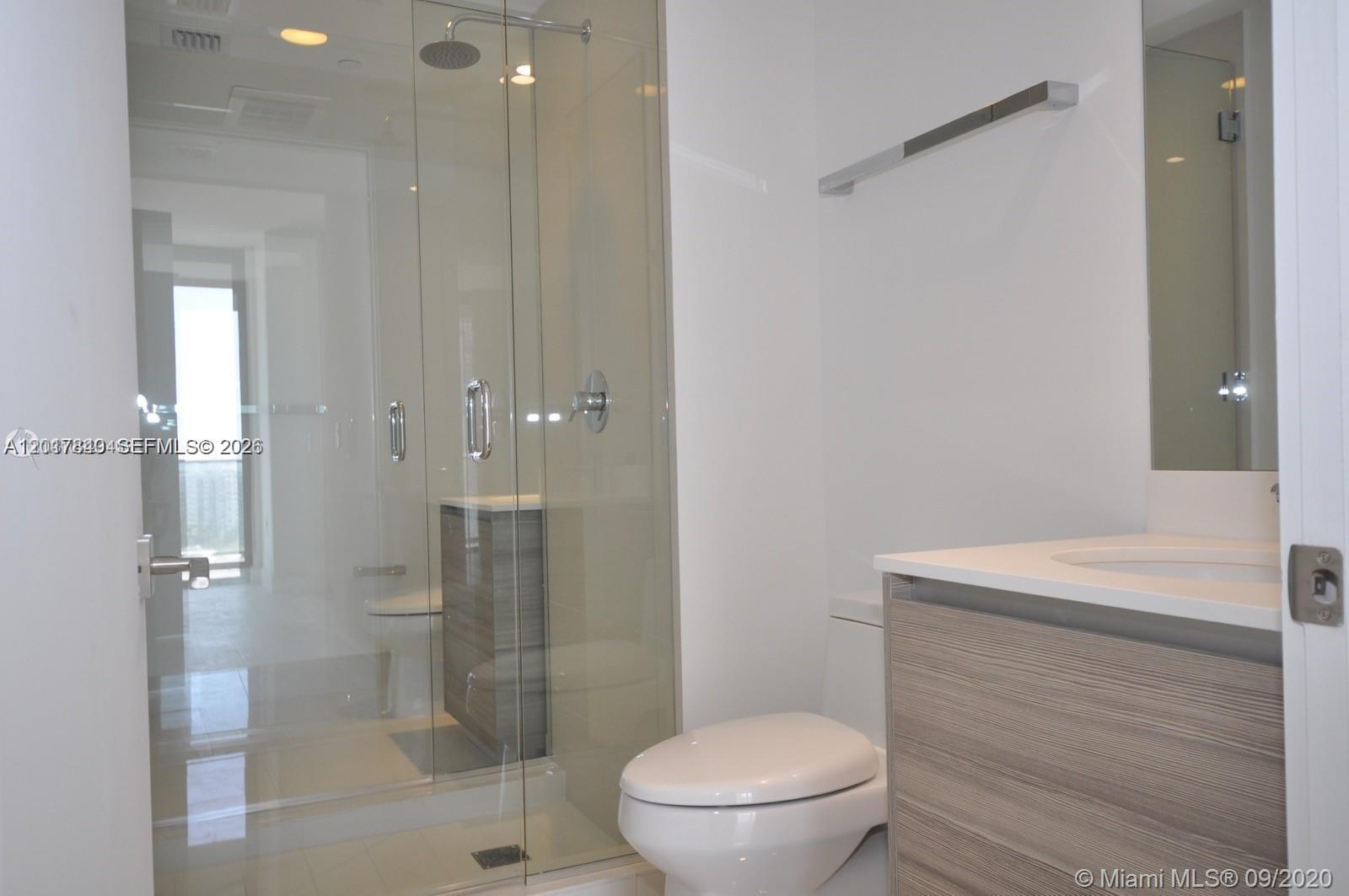 A modern bathroom features a glass-enclosed shower, a white toilet, and a wood-grain vanity — 121 NE 34th St # 806, Miami FL 33137, MIAMI, FL