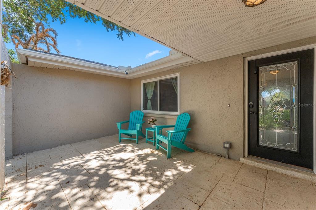 A covered patio features light-colored stone tiles, two turquoise chairs, and a glass-paneled front door — 1245 LESLIE DRIVE, MERRITT ISLAND, FL