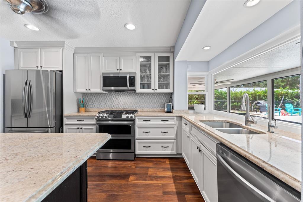 A kitchen features white cabinets, granite countertops, stainless steel appliances, and a large window view — 1245 LESLIE DRIVE, MERRITT ISLAND, FL
