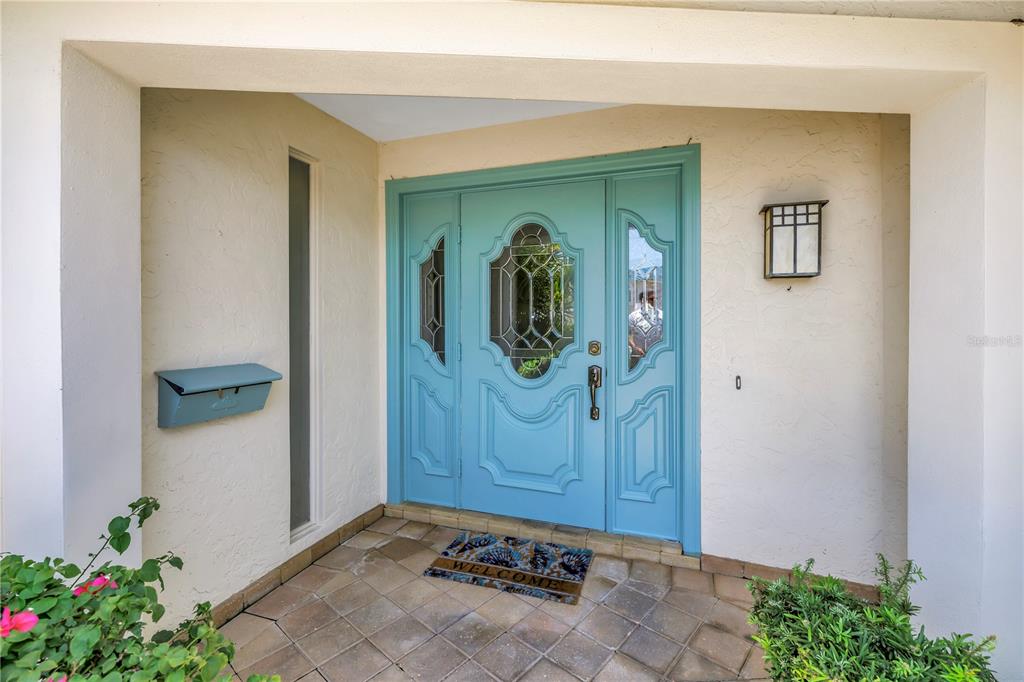 A light blue front door with glass inserts sits under a covered entryway — 2067 MASSACHUSETTS AVENUE NE, ST PETERSBURG, FL