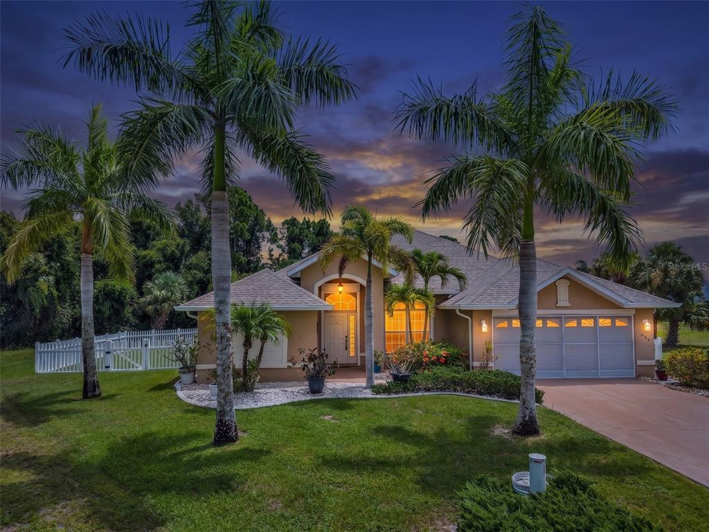 A single-story house with a two-car garage and palm trees at dusk — 608 TRUMPET TREE, PUNTA GORDA, FL