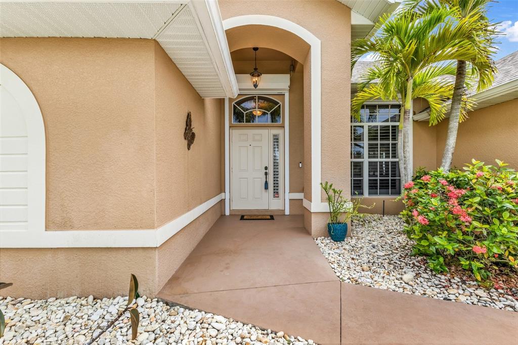 A beige house exterior features a covered entryway with a white door and palm trees — 608 TRUMPET TREE, PUNTA GORDA, FL