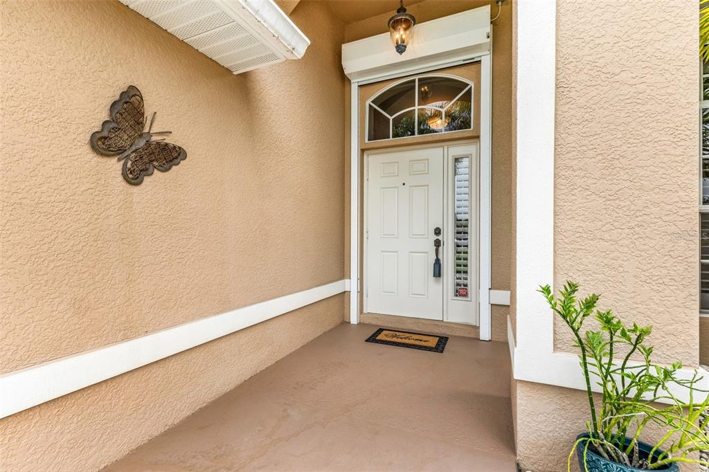 A covered entryway features a white front door with a sidelight and a butterfly wall decoration — 608 TRUMPET TREE, PUNTA GORDA, FL