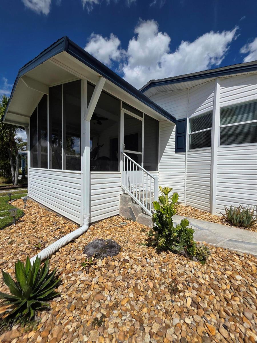 A white mobile home exterior features a screened-in porch, stone walkway, and gravel landscaping — 6469 Cypress Lane, Lantana FL 33462, LANTANA, FL