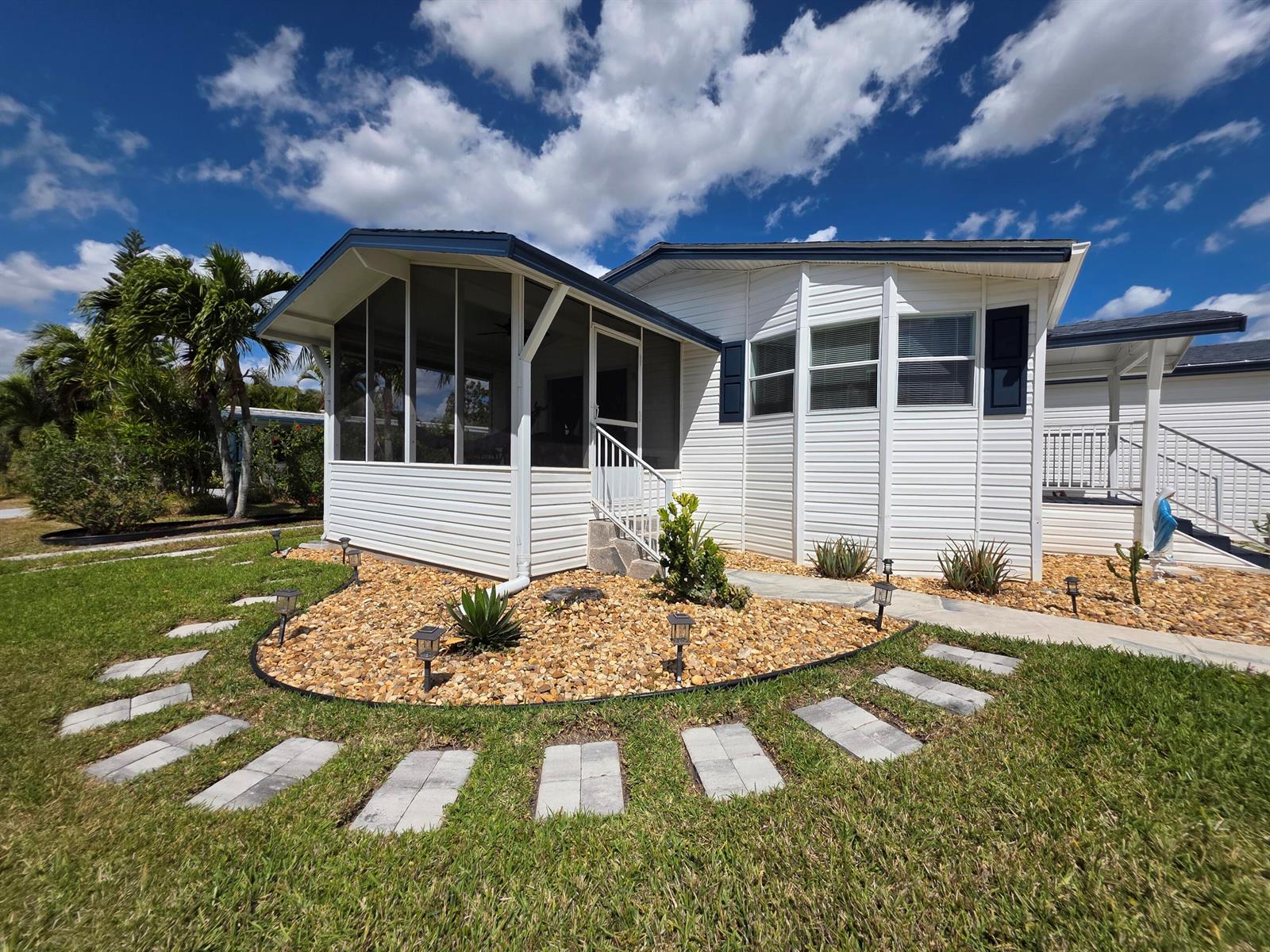 A white manufactured home features a screened-in porch, rock landscaping, and a stone walkway — 6469 Cypress Lane, Lantana FL 33462, LANTANA, FL