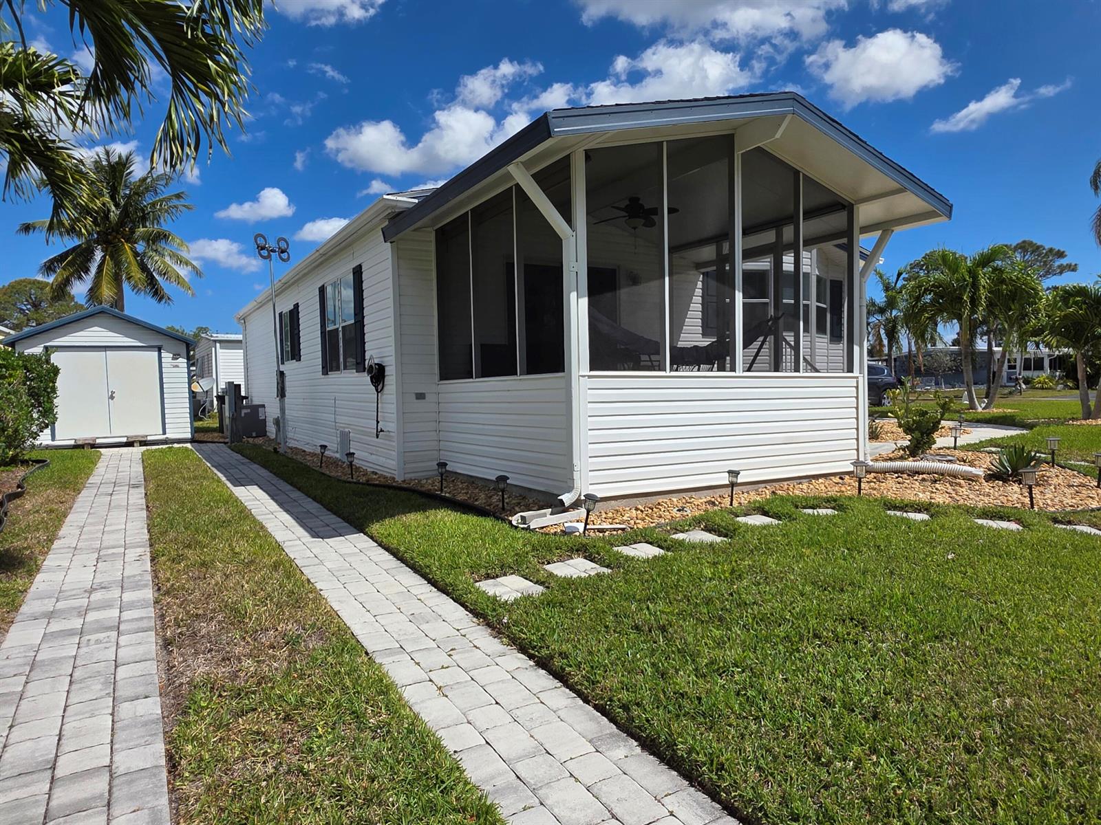 A white mobile home with a screened-in porch, a paved walkway, and a detached shed — 6469 Cypress Lane, Lantana FL 33462, LANTANA, FL
