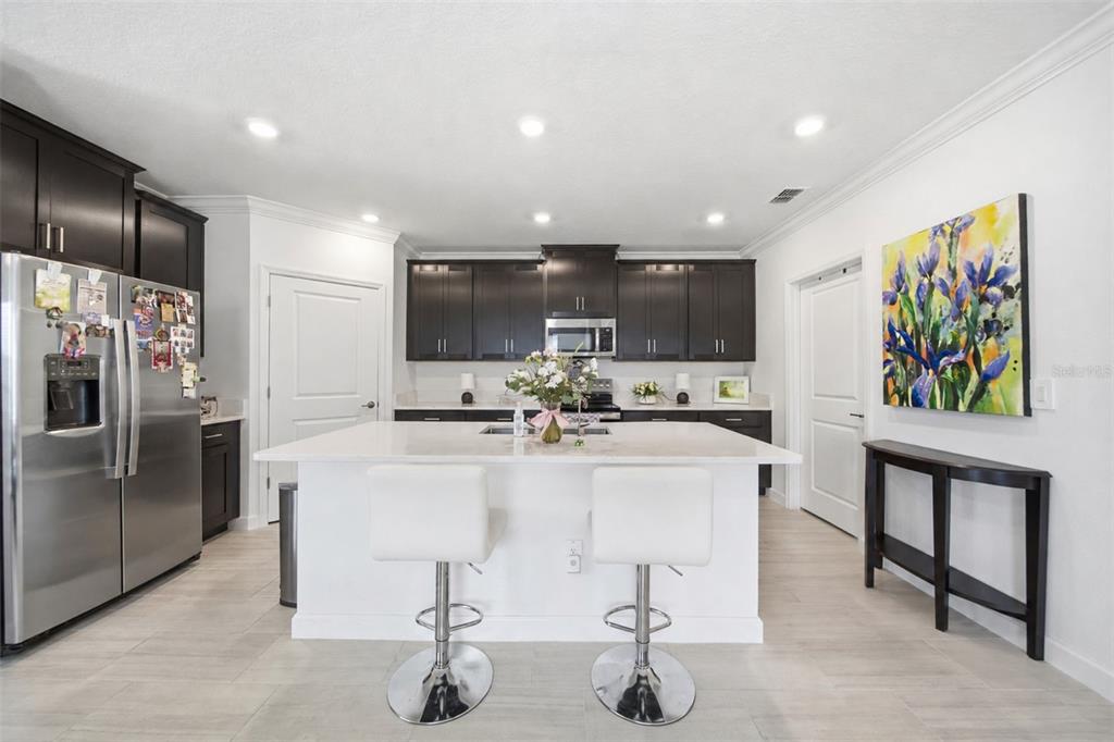 A modern kitchen features dark cabinets, a white island with two stools, and stainless appliances — 10834 GABLE DIG LOOP, SAN ANTONIO, FL