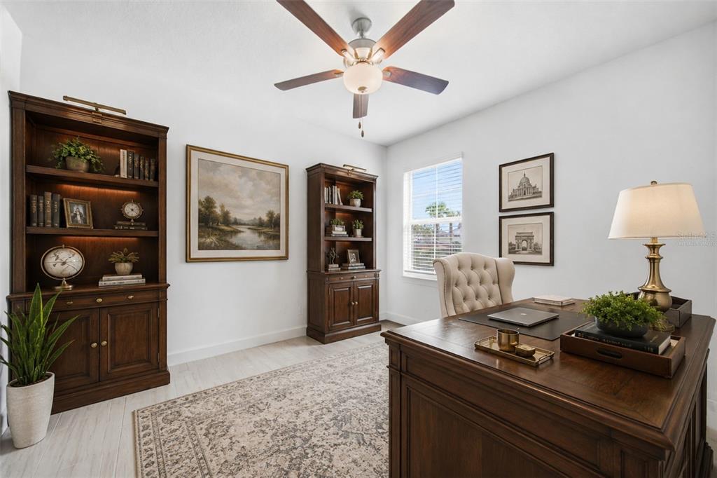 A home office features dark wood furniture, a tufted chair, and a patterned area rug — 10834 GABLE DIG LOOP, SAN ANTONIO, FL