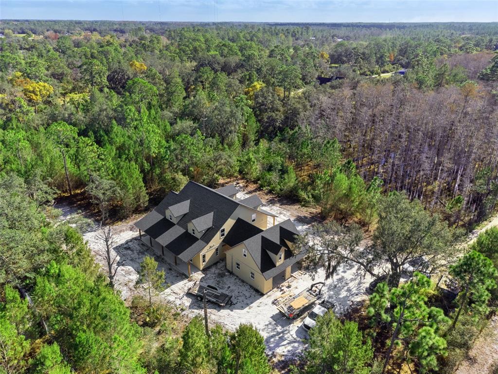 An aerial view shows a yellow house with a dark roof surrounded by dense forest — 490 RIVERWOODS TRAIL, CHULUOTA, FL