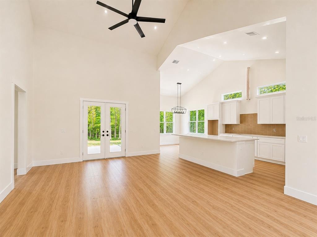 An open-concept living area features vaulted ceilings, light wood flooring, and a modern white kitchen — 490 RIVERWOODS TRAIL, CHULUOTA, FL