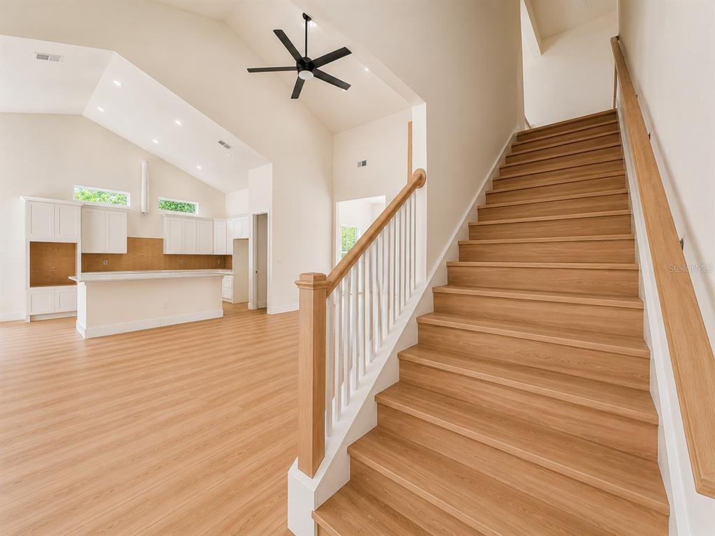 A bright open-concept kitchen with white cabinetry overlooks a staircase with light wood steps — 490 RIVERWOODS TRAIL, CHULUOTA, FL