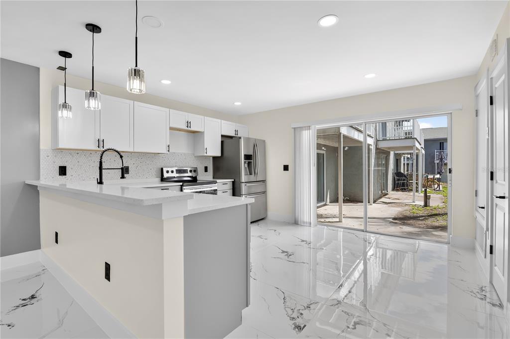 A modern kitchen features white cabinets, marble-look tile floors, and a sliding door to a patio — 3027 AARON BURR AVENUE UNIT L1, WINTER PARK, FL