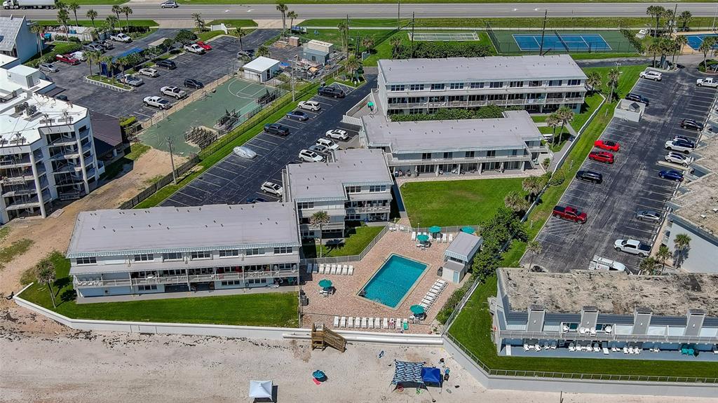 Aerial view of a beachside apartment complex with a swimming pool and parking lots — 4849 SAXON UNIT C202, NEW SMYRNA BEACH, FL