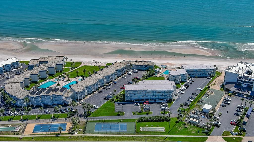 An aerial view shows a beachfront resort complex with multiple buildings, swimming pools, and tennis courts — 4849 SAXON UNIT C202, NEW SMYRNA BEACH, FL