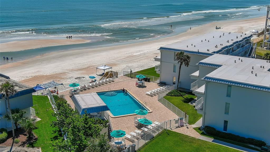 An aerial view shows a swimming pool and patio area adjacent to a beachside building — 4849 SAXON UNIT C202, NEW SMYRNA BEACH, FL