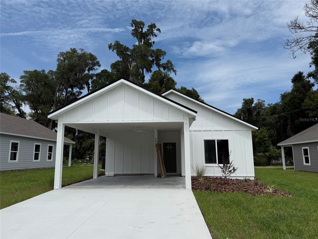 A white farmhouse-style house features a front carport, board-and-batten siding, and a dark front door — 2019 SE 45 TERRACE, GAINESVILLE, FL
