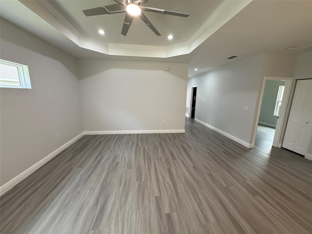 An empty room features gray wood-look flooring, a tray ceiling with a fan, and white walls — 2019 SE 45 TERRACE, GAINESVILLE, FL