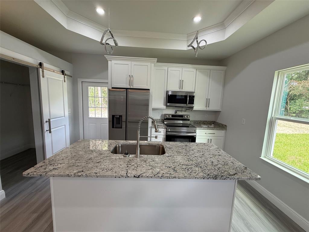 A kitchen features a granite-topped island, white cabinetry, stainless steel appliances, and a barn door — 2019 SE 45 TERRACE, GAINESVILLE, FL