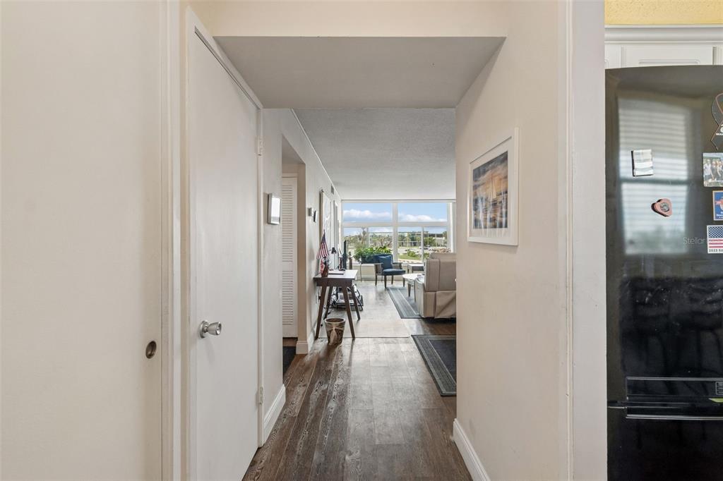 A hallway with wood-look flooring leads into a living area with large windows and furniture — 7465 BAY ISLAND DRIVE S UNIT 313, SOUTH PASADENA, FL