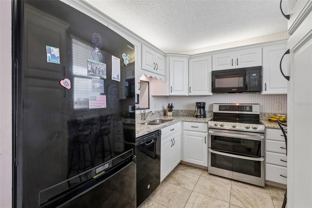 A kitchen featuring white cabinets, stainless steel appliances, a black refrigerator, and granite countertops — 7465 BAY ISLAND DRIVE S UNIT 313, SOUTH PASADENA, FL