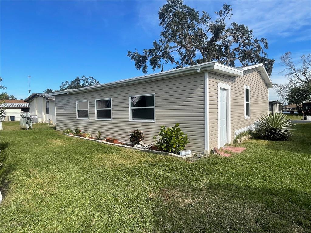 The exterior of a beige, single-story manufactured home features vinyl siding and a small garden — 3145 HIDDEN LAKE DRIVE, WESLEY CHAPEL, FL