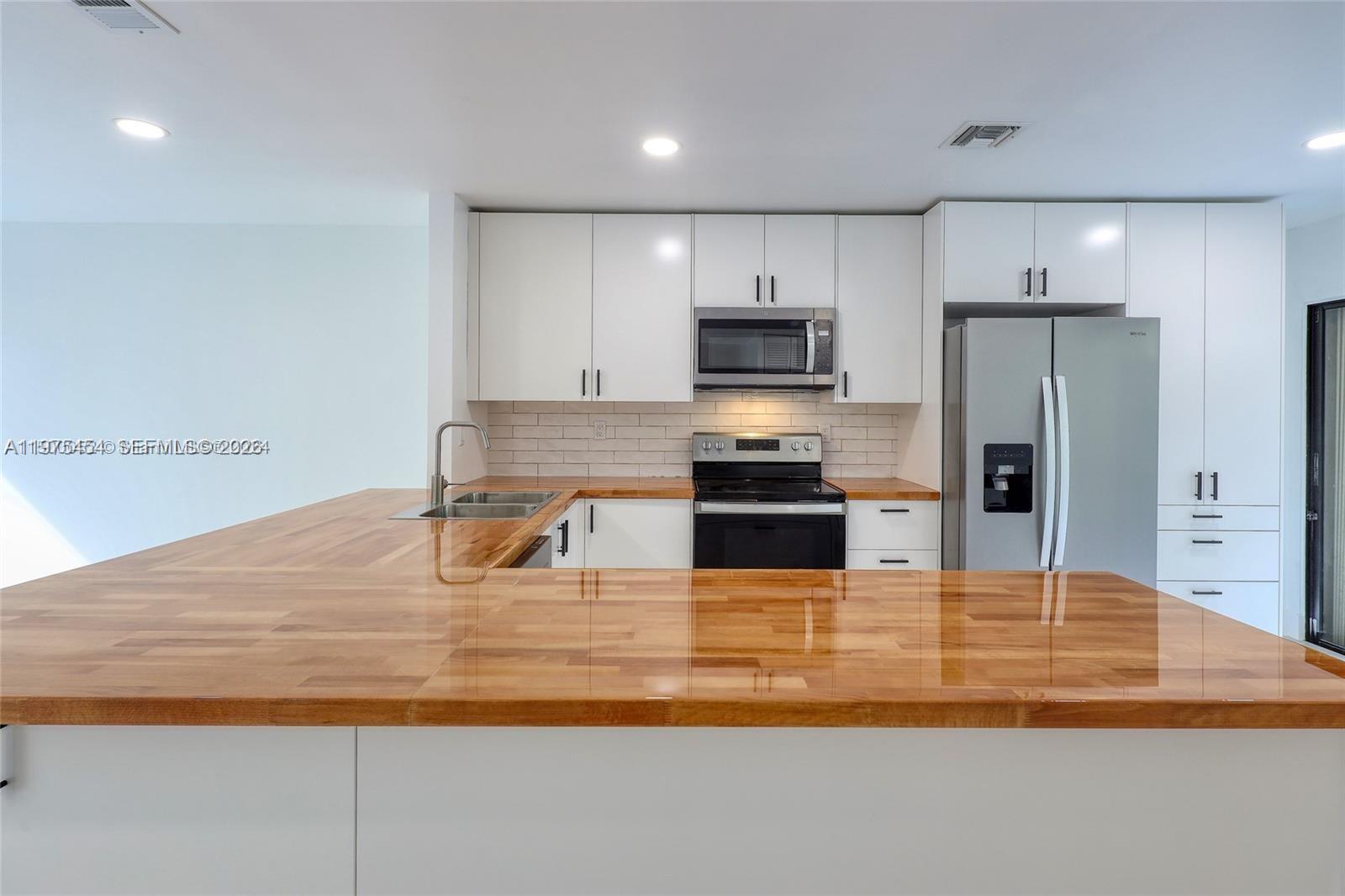 A kitchen features white cabinets, a stainless steel refrigerator, and a glossy wood countertop island — 3905 Adra Ave # 46B, Doral FL 33178, DORAL, FL