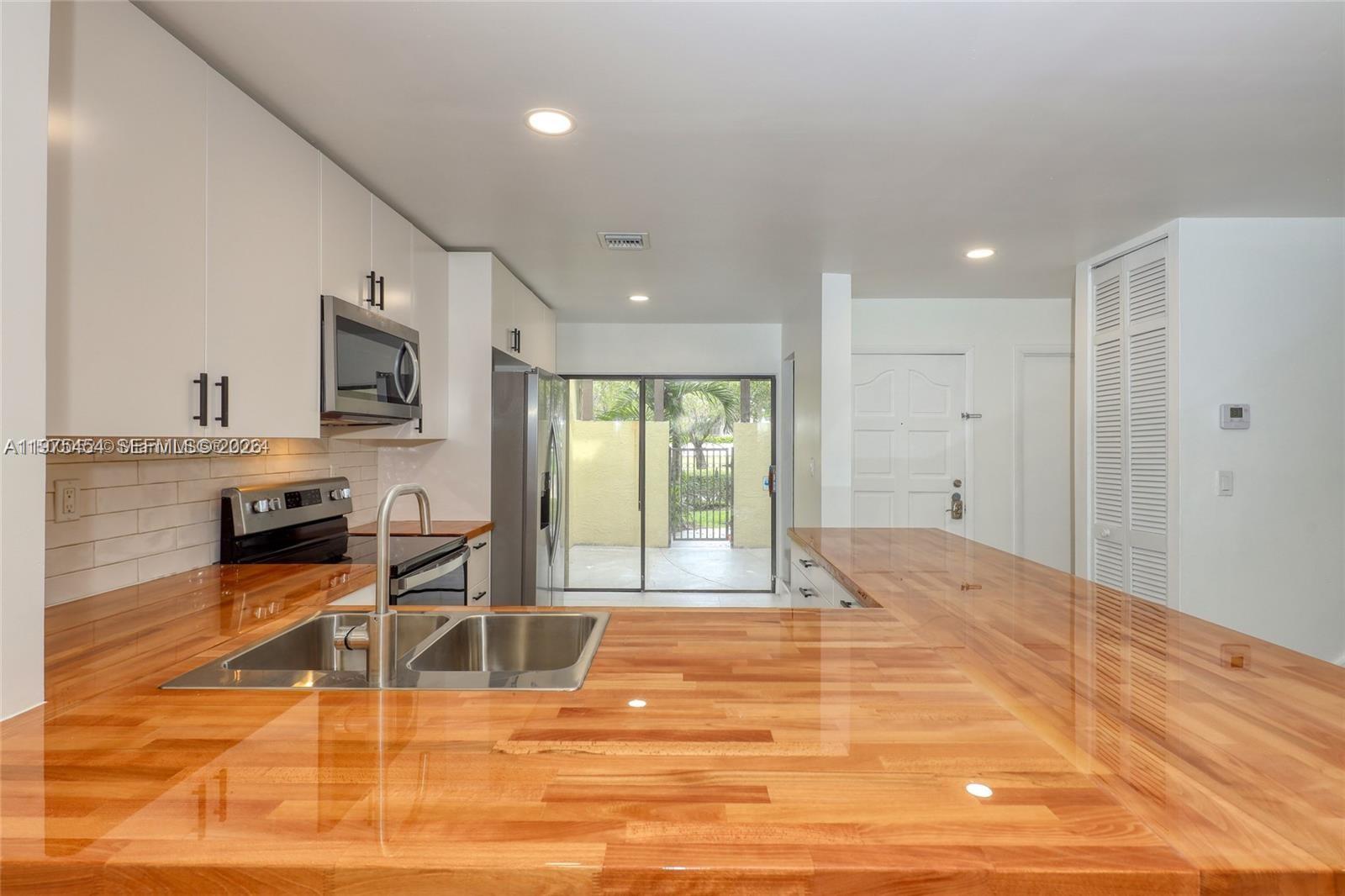 A kitchen features a wooden countertop, stainless steel sink, white cabinets, and a sliding glass door — 3905 Adra Ave # 46B, Doral FL 33178, DORAL, FL