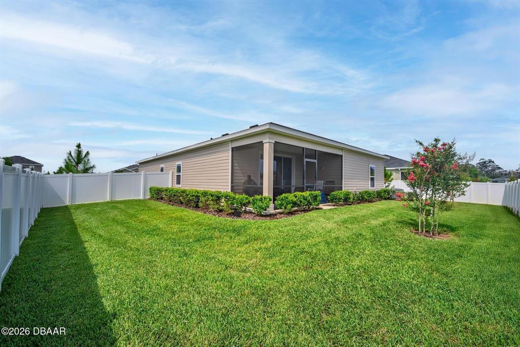 A beige house with a screened-in lanai sits in a backyard enclosed by white fencing — 4116 ACOMA DRIVE, ORMOND BEACH, FL