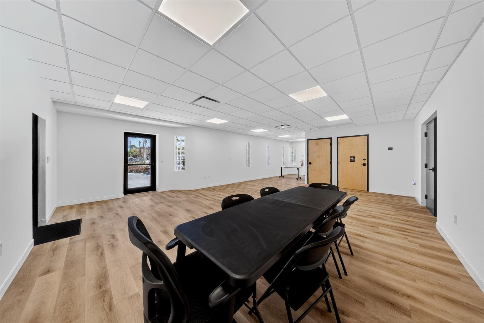 A bright, empty office space features a long black conference table, wood-look flooring, and drop-ceiling tiles — 405 Angle Road, Fort Pierce FL 34947, FORT PIERCE, FL