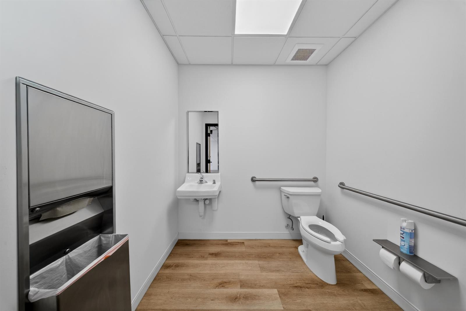 A modern, accessible restroom features a white toilet, wall-mounted sink, and light wood-look flooring — 405 Angle Road, Fort Pierce FL 34947, FORT PIERCE, FL