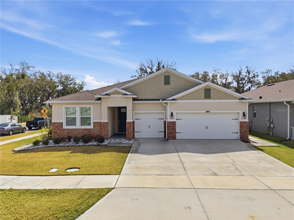 A single-story house with a three-car garage, stone accents, and a beige exterior — 1636 BARBERRY DRIVE, KISSIMMEE, FL