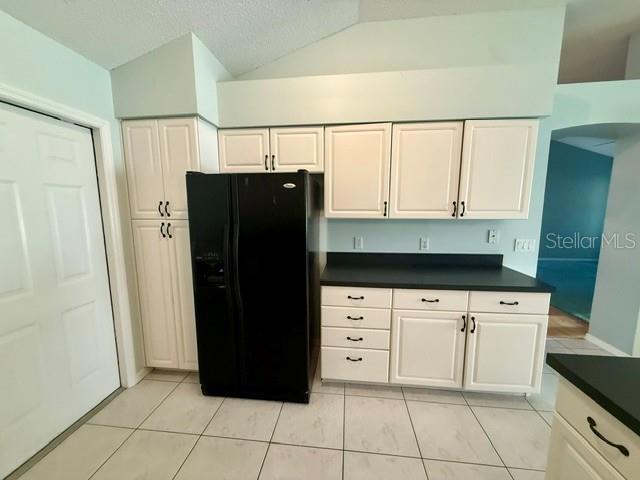 A kitchen features white cabinets, a black refrigerator, and a dark countertop on tiled floors — 724 VISTA PLACE, LADY LAKE, FL