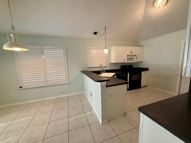 A kitchen features white cabinets, black countertops, tile flooring, and a breakfast bar — 724 VISTA PLACE, LADY LAKE, FL