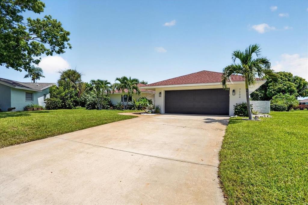 A single-story house with a large concrete driveway, a two-car garage, and surrounding palm trees — 7204 13TH AVENUE W, BRADENTON, FL