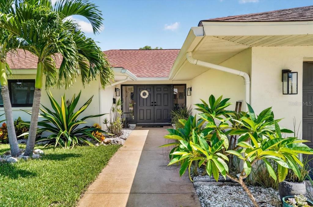 A concrete walkway leads to the dark double front doors of a single-story house — 7204 13TH AVENUE W, BRADENTON, FL