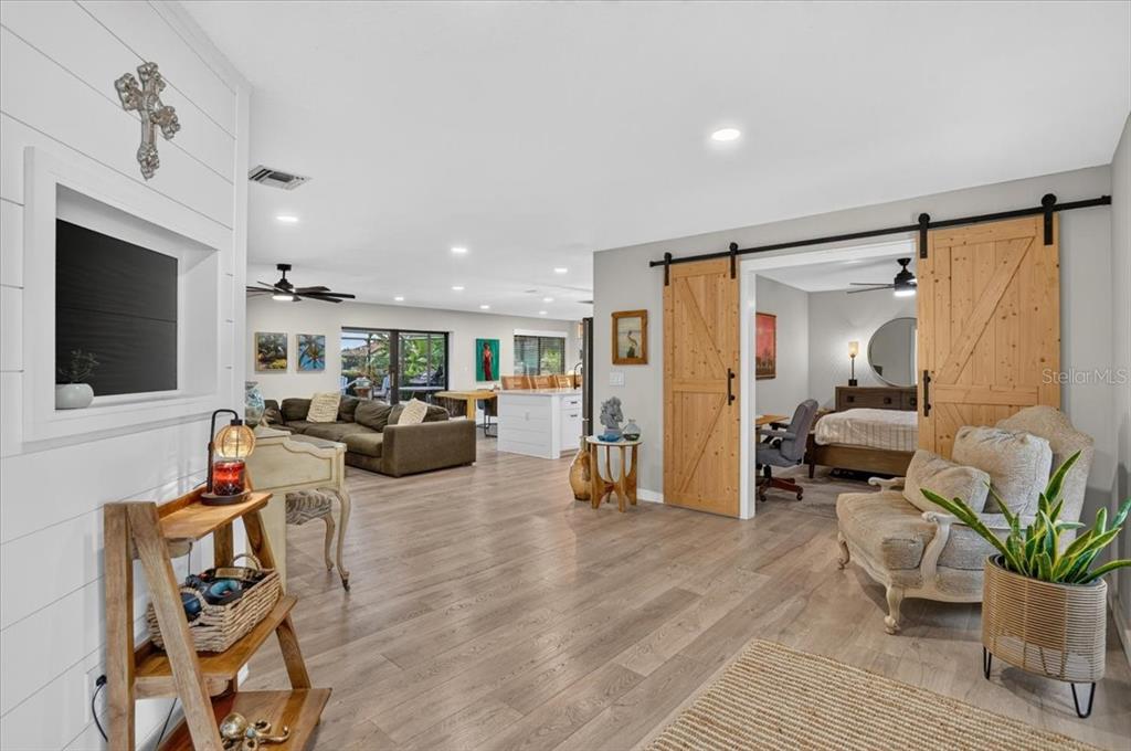 An open-concept living area features wood-look flooring, a sliding barn door, and a kitchen beyond — 7204 13TH AVENUE W, BRADENTON, FL