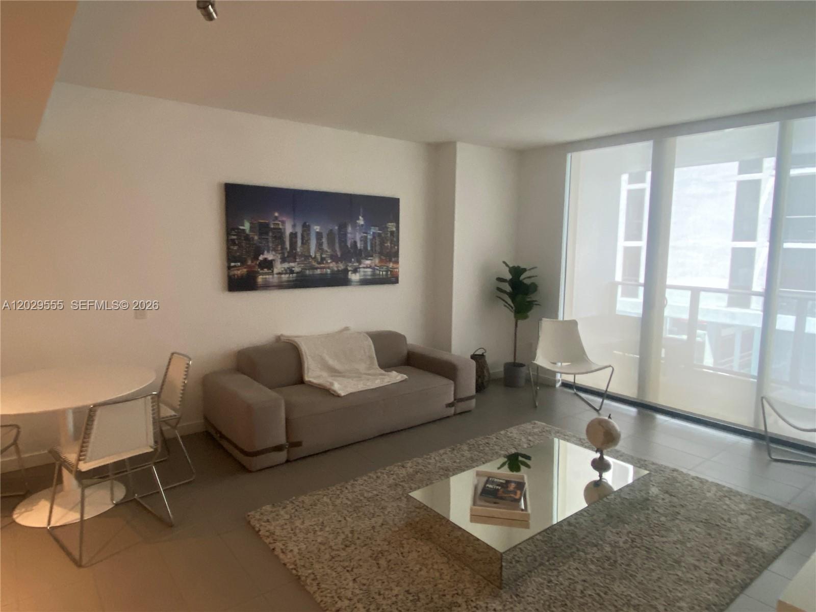 A living room features a gray sofa, a mirrored coffee table, and floor-to-ceiling windows — 1600 NE 1st Ave # 1117, Miami FL 33132, MIAMI, FL