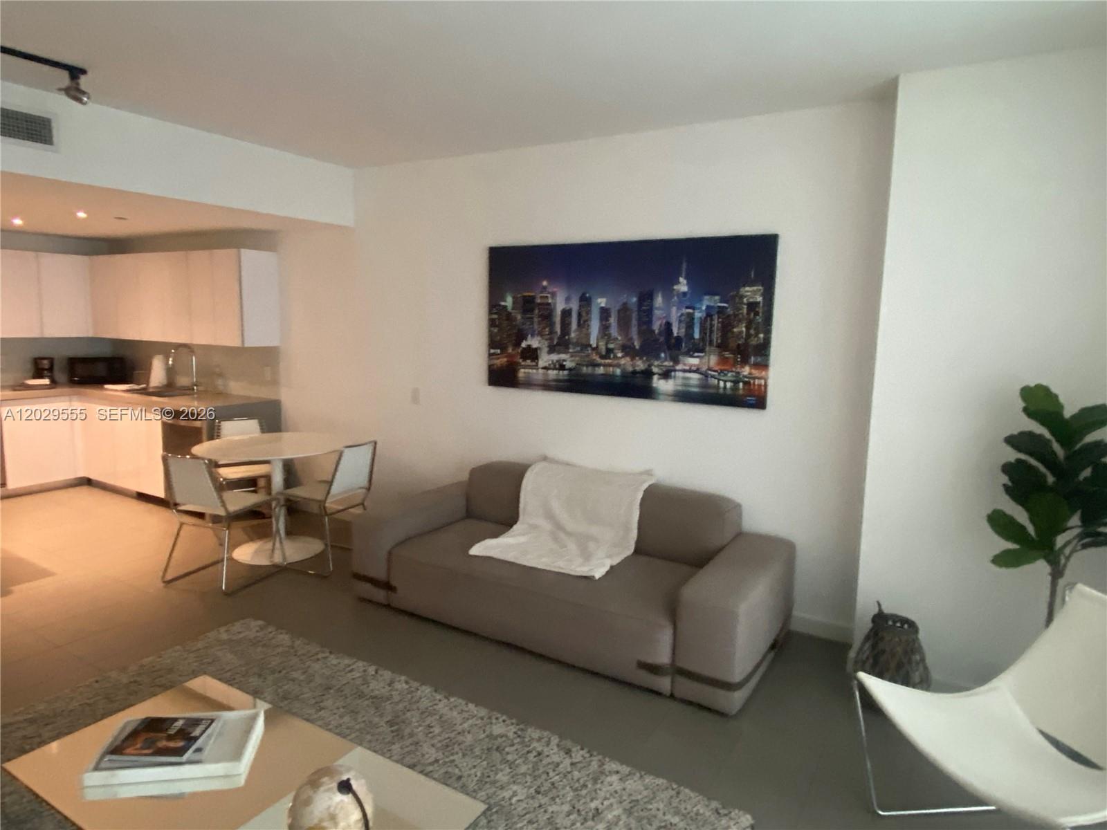 A living room features a gray sofa, a dining table, and a city skyline wall art — 1600 NE 1st Ave # 1117, Miami FL 33132, MIAMI, FL