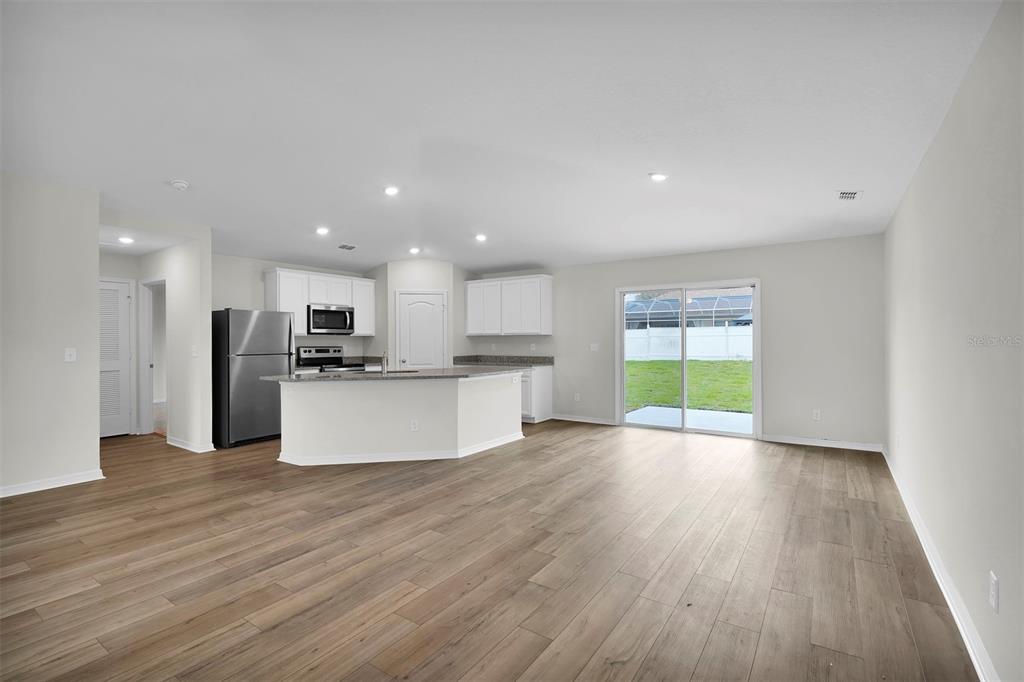 An open-concept kitchen and living area with wood-look flooring, white cabinets, and sliding glass doors — 57 PRITCHARD DRIVE, PALM COAST, FL
