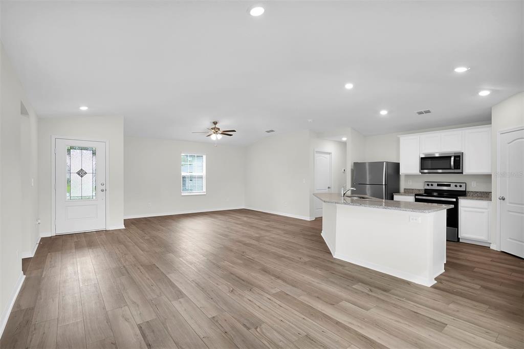An open-concept kitchen and living area featuring white cabinets, stainless steel appliances, and wood-look flooring — 57 PRITCHARD DRIVE, PALM COAST, FL