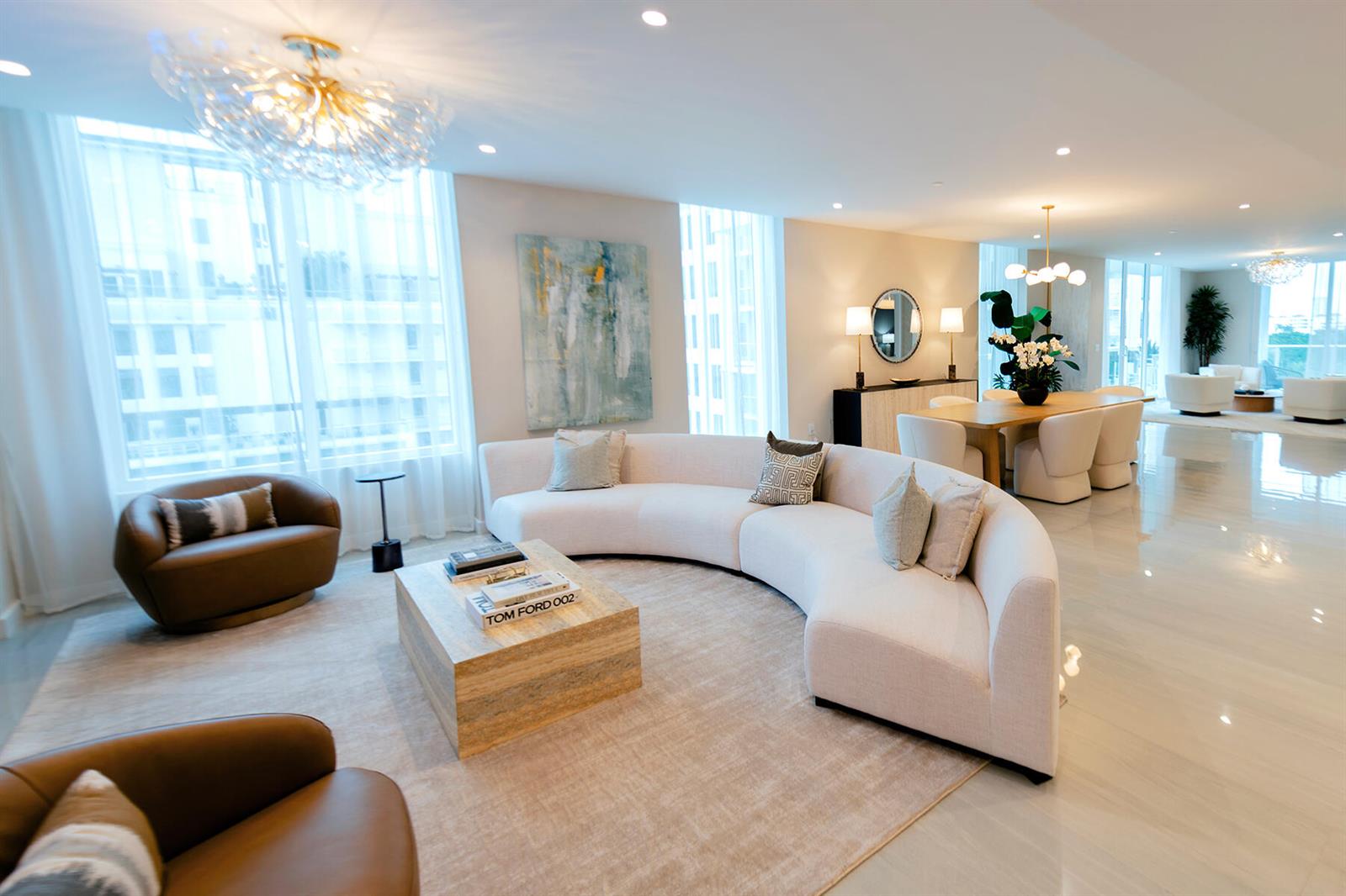 A spacious, modern living and dining area features a curved sofa, neutral tones, and lighting — 220 SE Mizner Boulevard # 501, Boca Raton FL 33432, BOCA RATON, FL