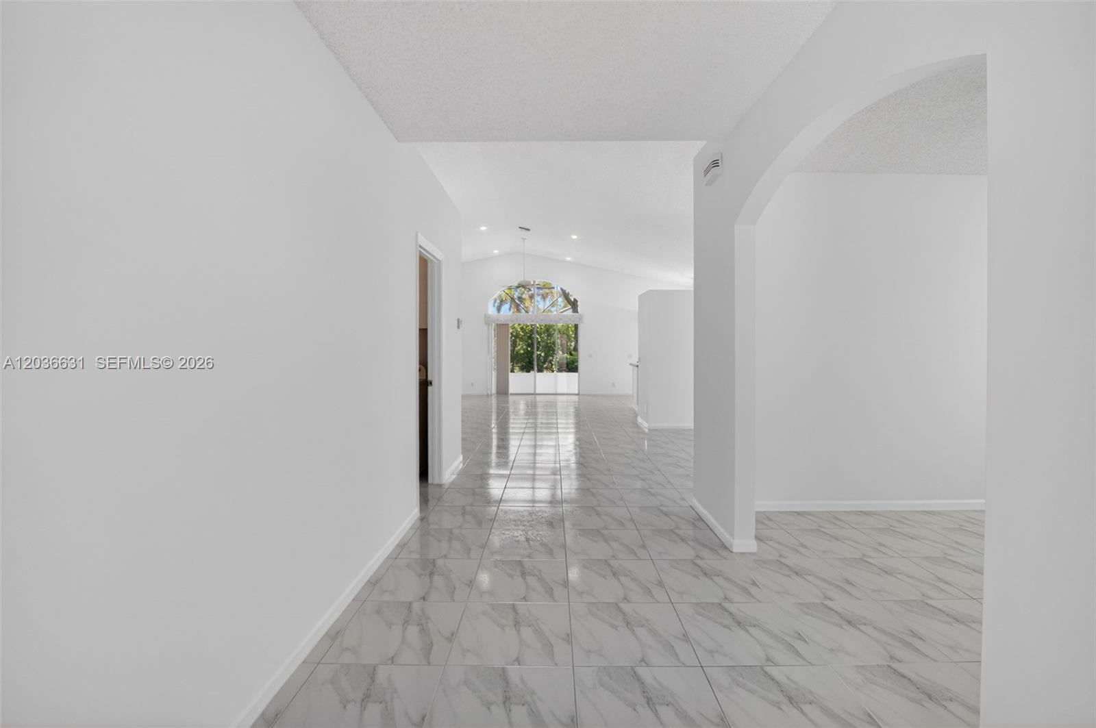 A bright hallway with white walls and light-colored marble-patterned tile flooring leads toward a living area — 7679 Lemonwood St, Boynton Beach FL 33437, BOYNTON BEACH, FL