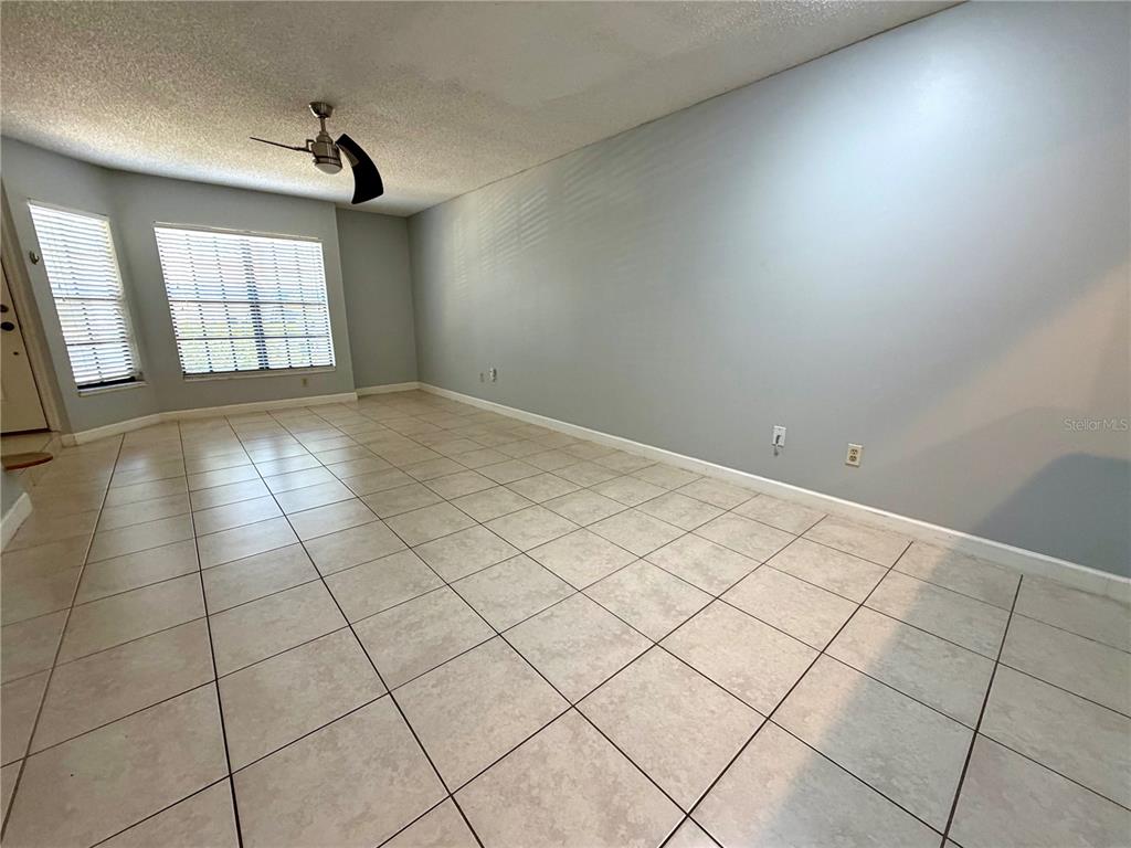 An empty room features light-colored tile flooring, a ceiling fan, and large windows with blinds — 5100 BURCHETTE ROAD UNIT 3102, TAMPA, FL