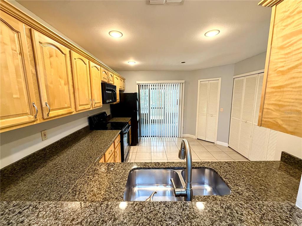 A kitchen features light wood cabinets, granite countertops, a double sink, and tile flooring — 5100 BURCHETTE ROAD UNIT 3102, TAMPA, FL
