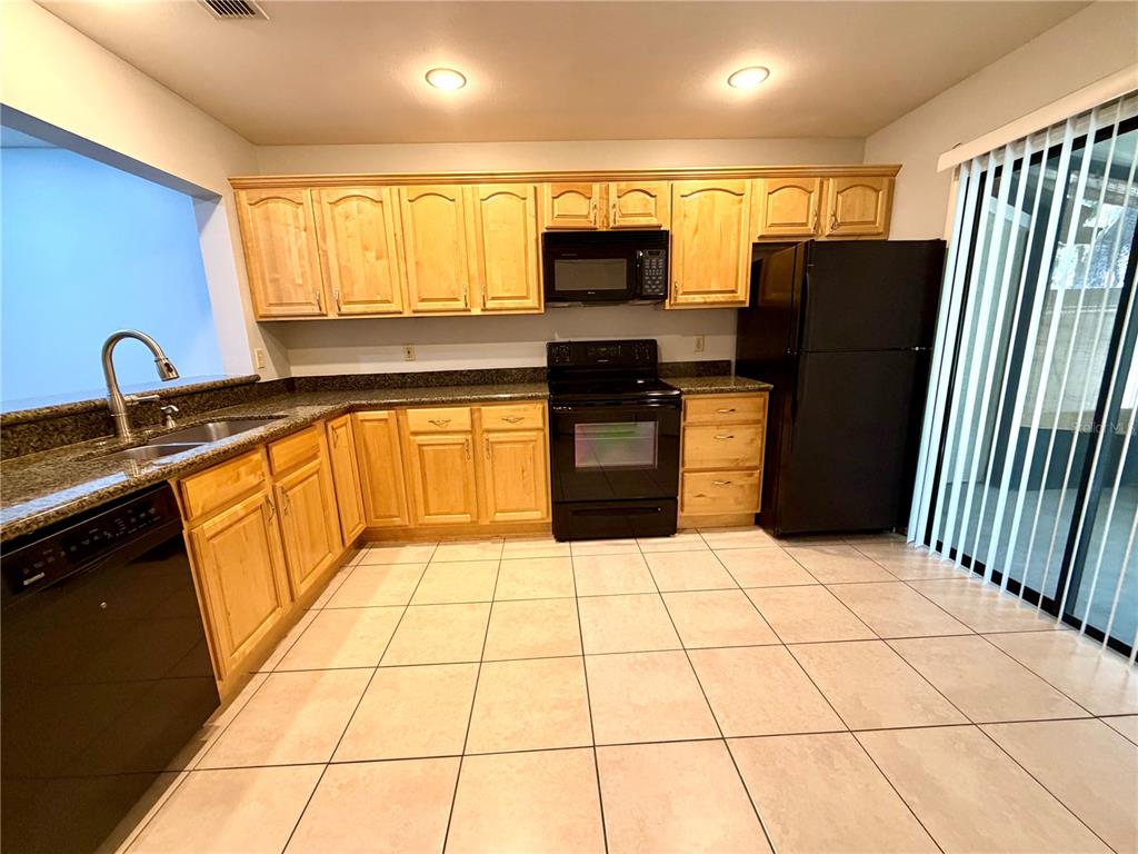 A kitchen features light wood cabinets, black appliances, dark granite countertops, and light tile flooring — 5100 BURCHETTE ROAD UNIT 3102, TAMPA, FL