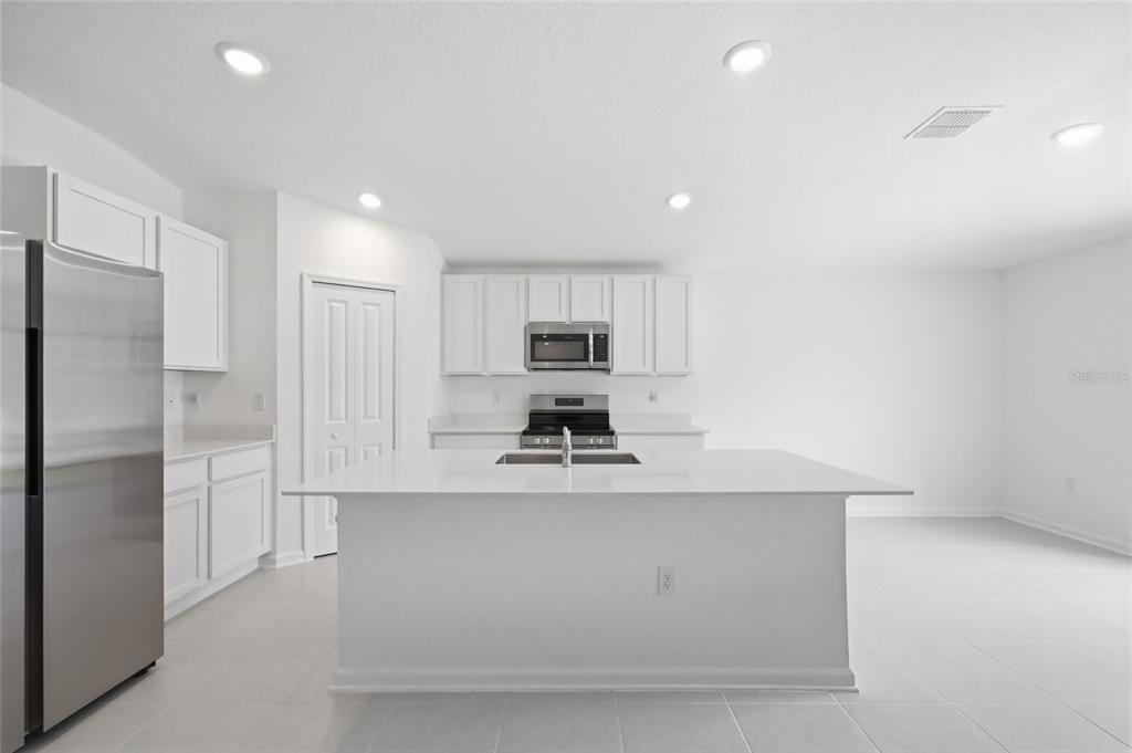 A modern kitchen features white cabinets, stainless steel appliances, and a large central island — 1251 INKBERRY CIRCLE, DELAND, FL