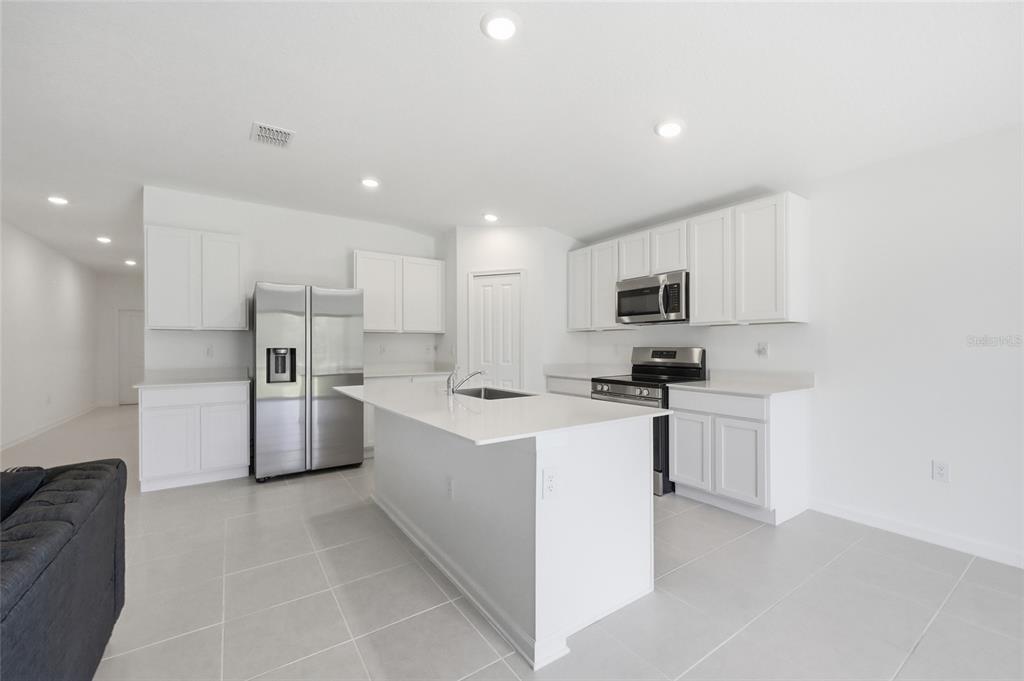 A modern kitchen features white cabinets, stainless steel appliances, a center island, and tile flooring — 1251 INKBERRY CIRCLE, DELAND, FL