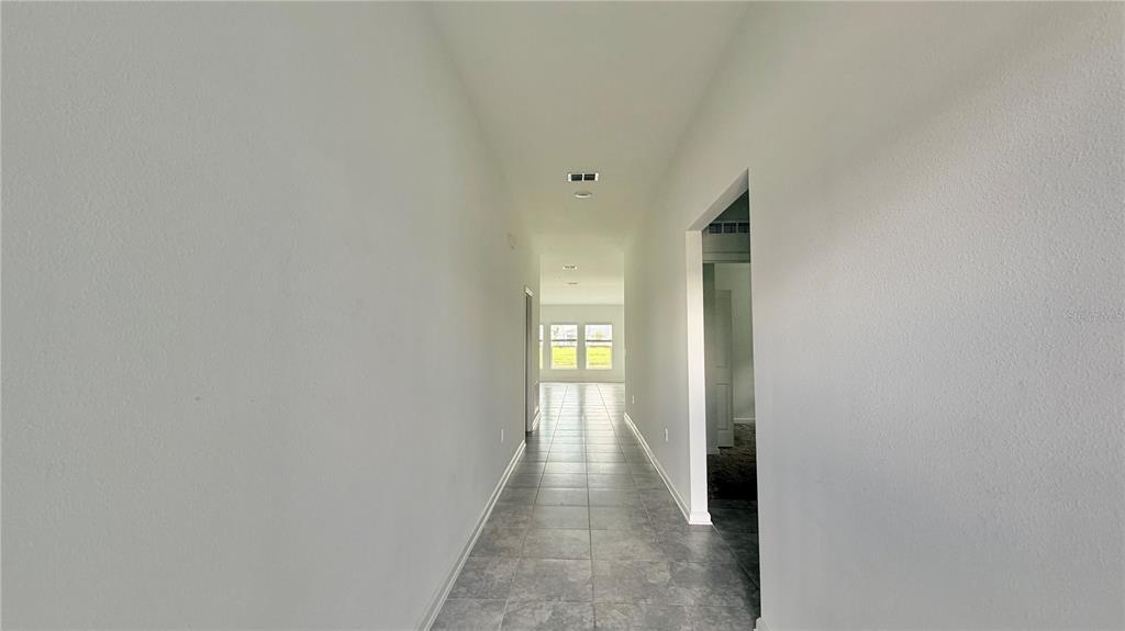 A long, tiled hallway leads to a windowed room with light gray walls — 5768 GINGHAM DRIVE, KISSIMMEE, FL