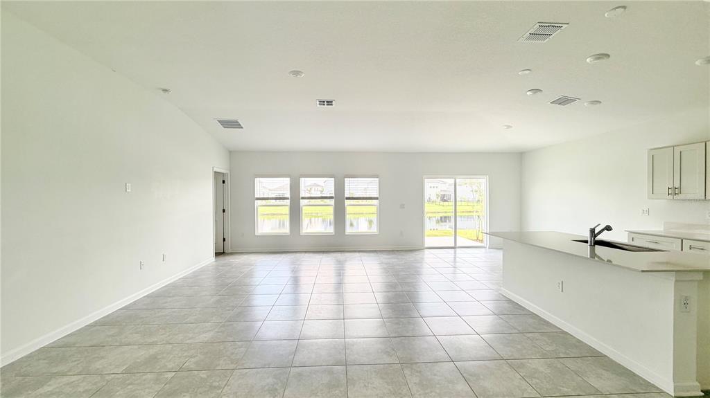 A spacious, open-concept living area features light tile flooring, white walls, and a kitchen island — 5768 GINGHAM DRIVE, KISSIMMEE, FL