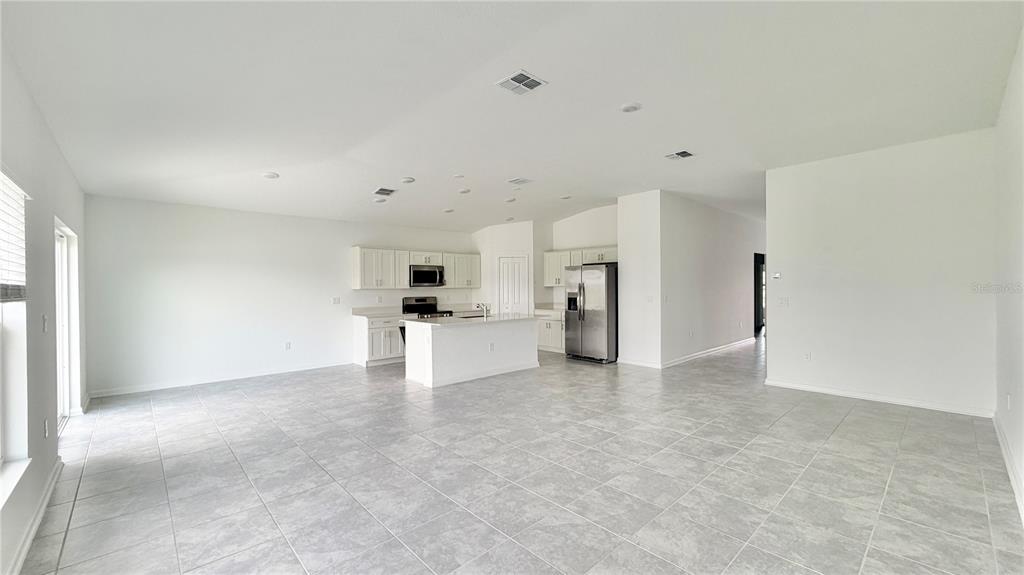 An open-concept kitchen and living area featuring white cabinets, stainless appliances, and tile flooring — 5768 GINGHAM DRIVE, KISSIMMEE, FL